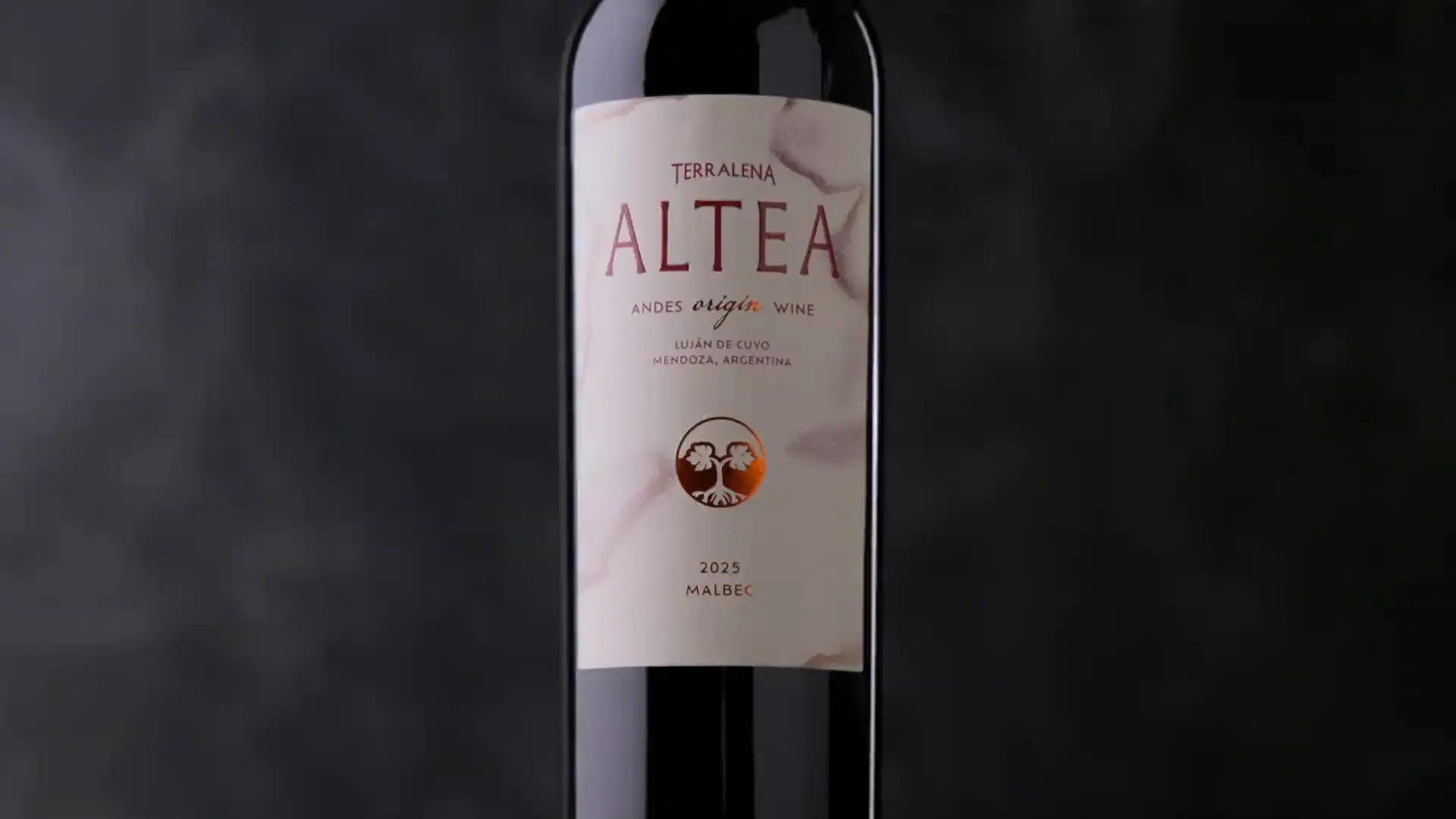 Una botella de Altea Origin junto a copas de vino tinto, frente a una chimenea encendida