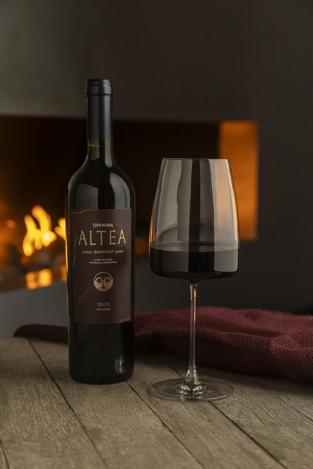 Una botella de Altea Reserve y una copa servida junto al fuego