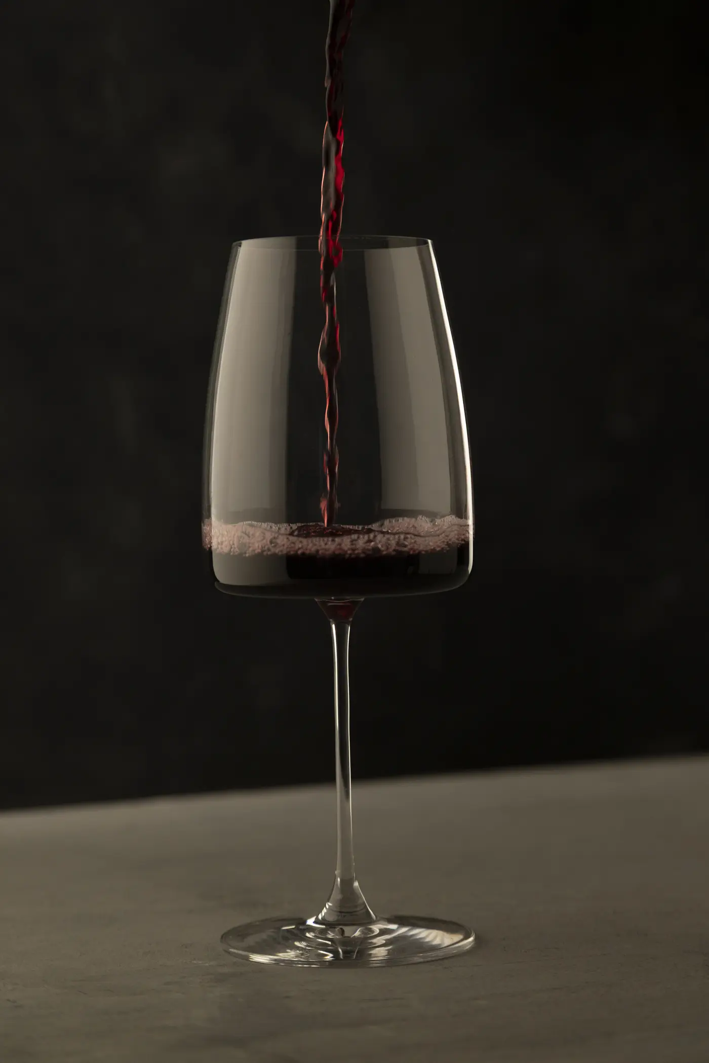 Vino tinto sirviéndose en una copa, sobre fondo oscuro