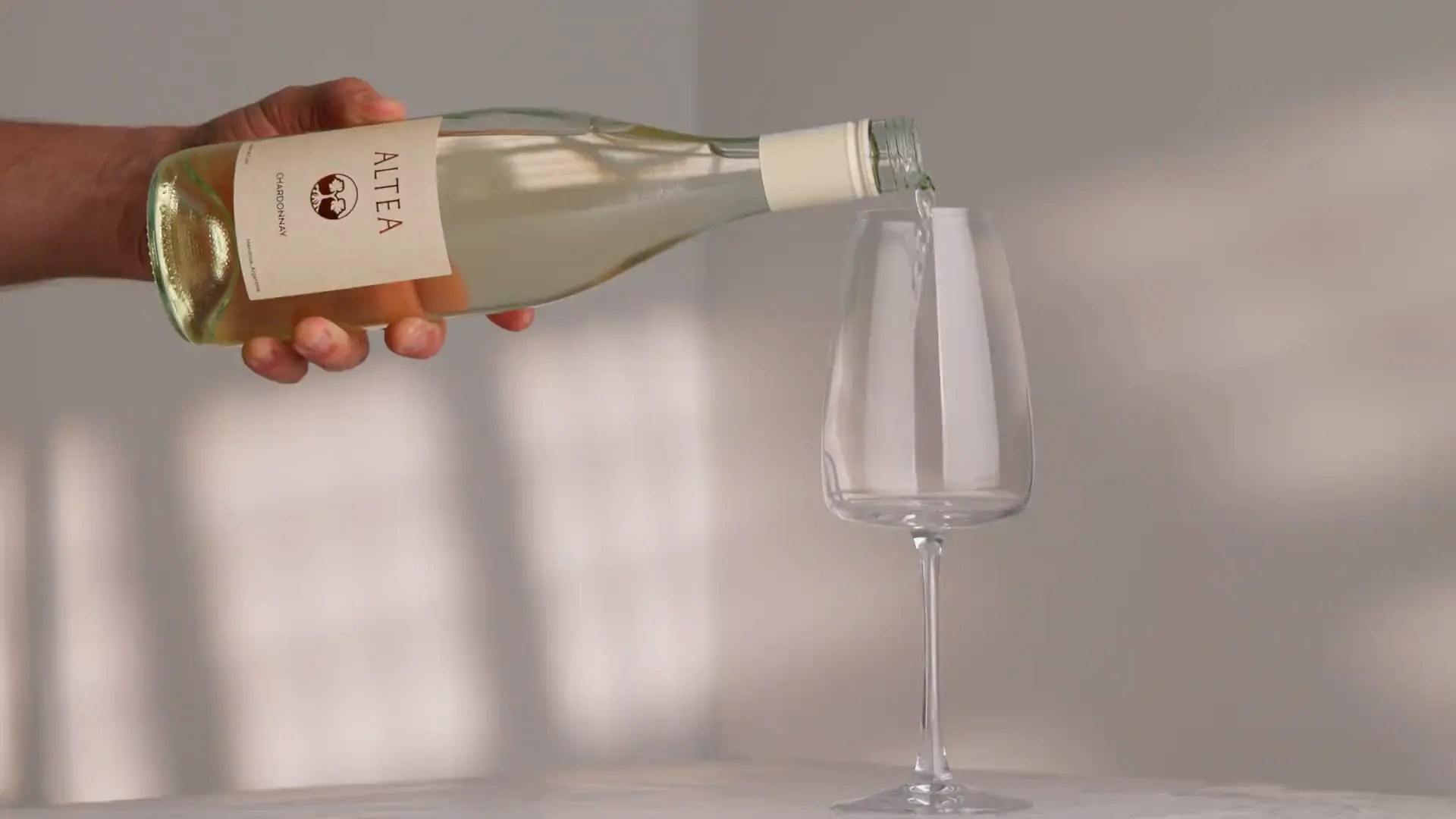 Una mano sirve Altea Chardonnay en una copa, con la luz de una ventana sobre la pared